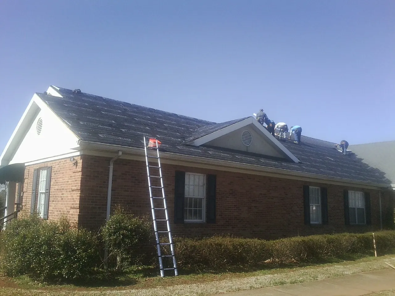 Crew tearing shingles off a brick ranch roof with a ladder set — Emergency Roof Repair work by our crew in Rothsay