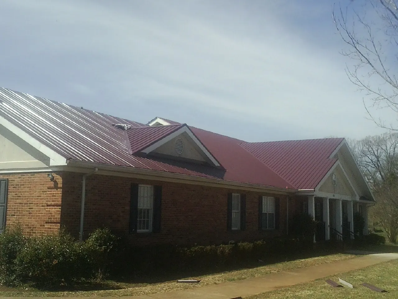 Red metal roof with gabled entries on a long brick building, from a Hail Damage Roof Repair job in Rothsay