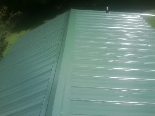 New green metal panels meeting at the ridge of a roof — Flat Roof Repair work by our crew in Rothsay