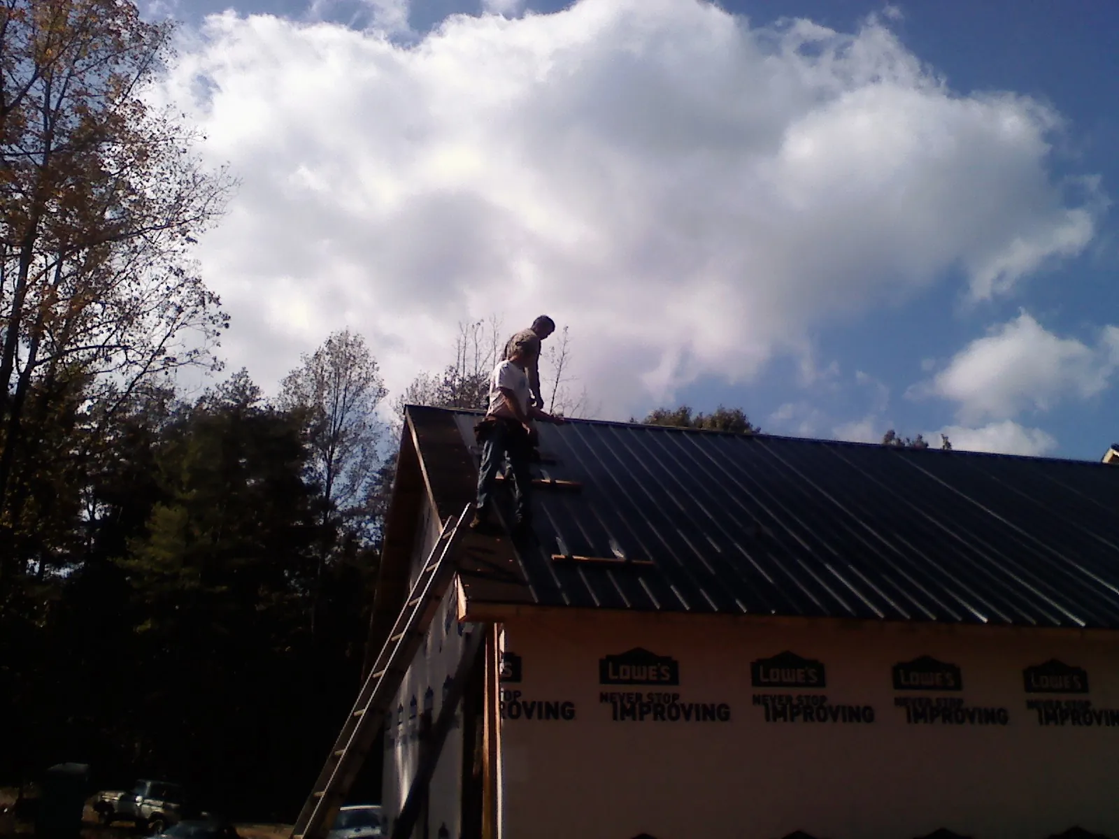 Roofer fastening dark metal panels high against a cloudy sky, from a Roof Inspection job in Rothsay