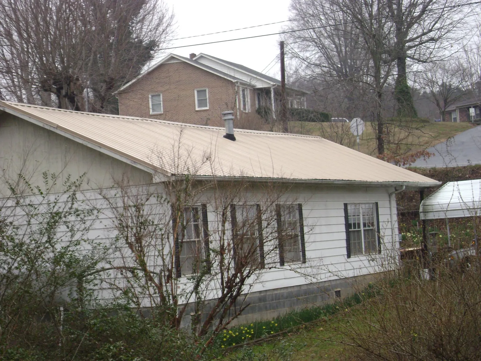 Tan metal roof on a white sided house set into a hillside — Commercial Roofing by Roofing Brothers in Rothsay